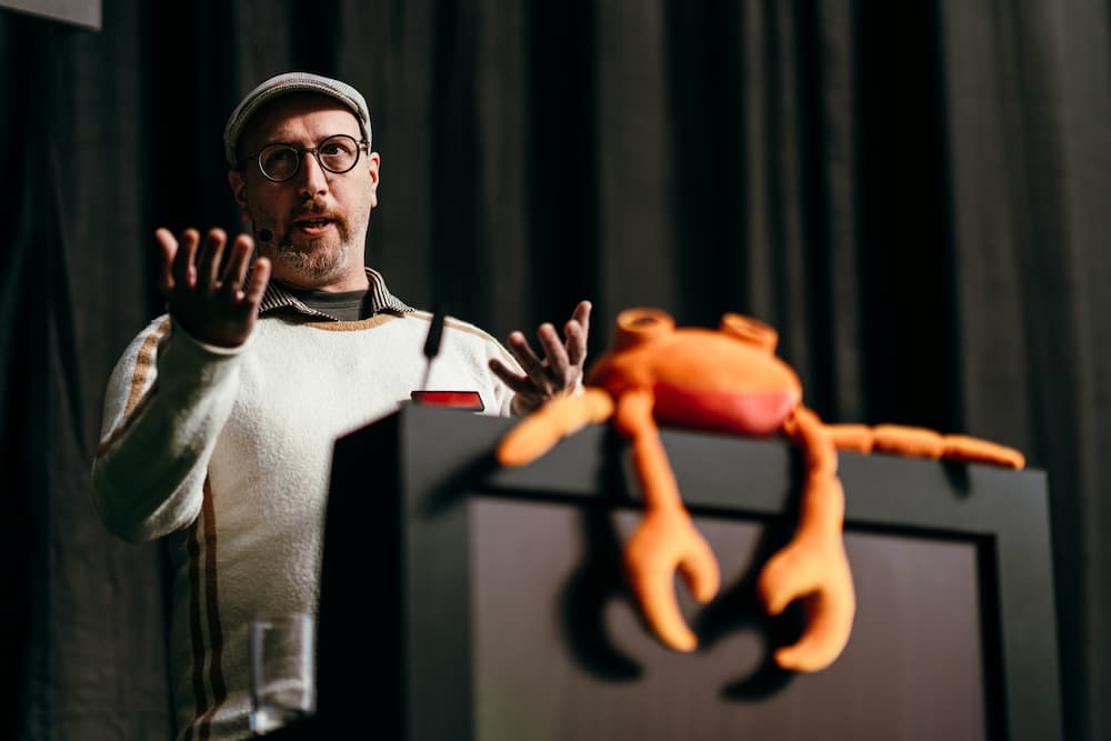 Daniel presenting on stage, with a Nova (crab mascot) plushie on the podium.