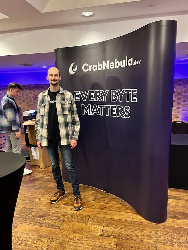 Robin standing in front of a large banner that says "CrabNebula. Every byte matters."